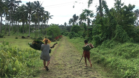 Two people walk five feet apart down a grassy pathway as they carry materials