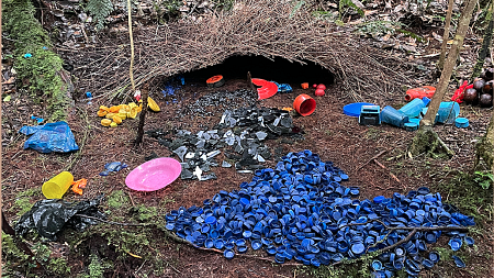 Colorful plastic pieces surround a small straw dwelling in a nestlike arrangement