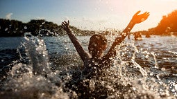 A child gleefully splashes water as they swim in a lake surrounded by mountains.