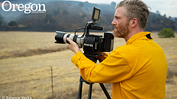 "Elemental" filmmaker Trip Jennings looks through a viewfinder on a camera that faces a field and is fixed to a tripod. 