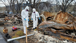 Two disaster workers walk through and examine the aftermath of an out-of-control fire. 