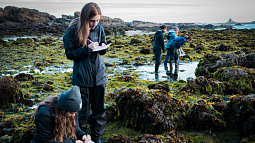 Marine biology students observe tide pools and take notes. 