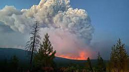 Wildfire smoke fills the sky as a mountainside burns
