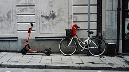 On a sidewalk, a bike and scooter lean against the outer wall of a building. Photo by Gemma Evans/Unsplash