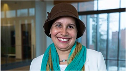 Dr. Alaí Reyes-Santos wears a brown hat and colorful scarf andflashes a wide smile